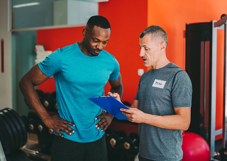 two men discussing workout in gym