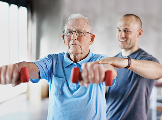 physical therapist helping senior patient lift weights