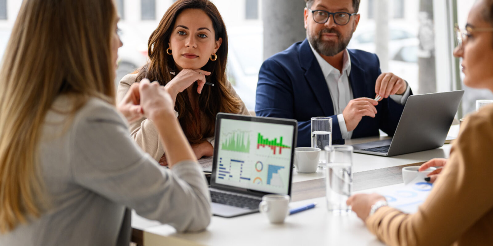 Business team engaged in a data analytics meeting around a conference table with laptop displaying charts and graphs